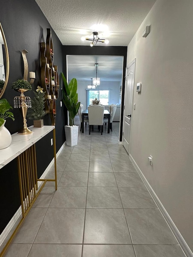 hallway featuring tile patterned flooring, a textured ceiling, and a notable chandelier