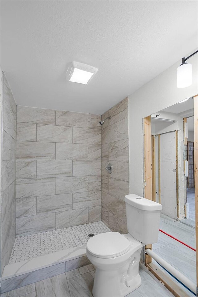 bathroom featuring a tile shower, a textured ceiling, and toilet