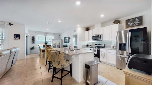 kitchen featuring a center island with sink, light stone countertops, light tile patterned floors, white cabinetry, and stainless steel appliances