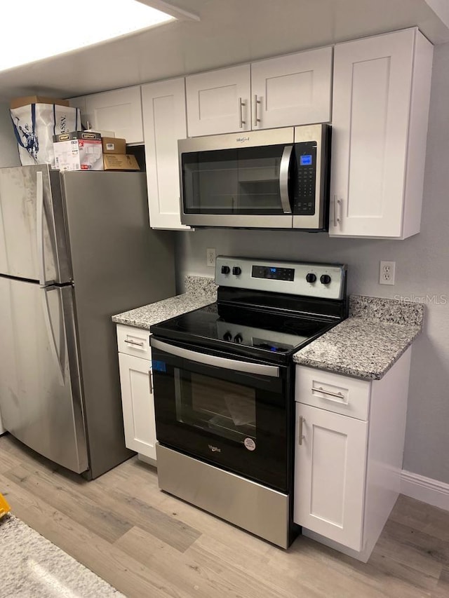 kitchen with white cabinets, light stone countertops, appliances with stainless steel finishes, and light hardwood / wood-style flooring