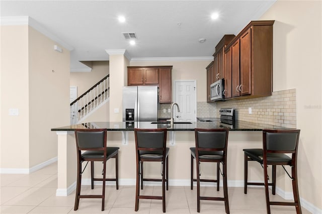 kitchen featuring appliances with stainless steel finishes, dark stone counters, sink, light tile patterned floors, and a breakfast bar area