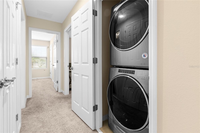 clothes washing area featuring stacked washing maching and dryer and light carpet