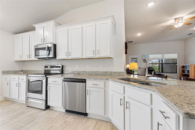 kitchen with kitchen peninsula, appliances with stainless steel finishes, vaulted ceiling, sink, and white cabinets