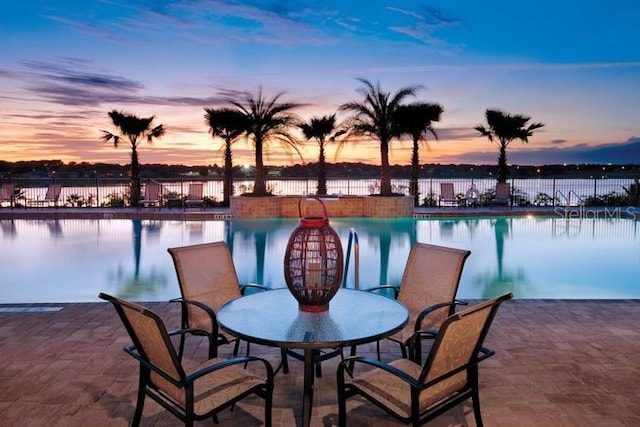 patio terrace at dusk with a community pool and a water view