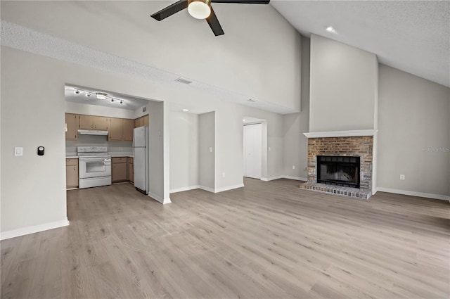 unfurnished living room with ceiling fan, a brick fireplace, lofted ceiling, a textured ceiling, and light wood-type flooring