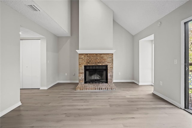 unfurnished living room featuring a textured ceiling, light hardwood / wood-style floors, a brick fireplace, and lofted ceiling