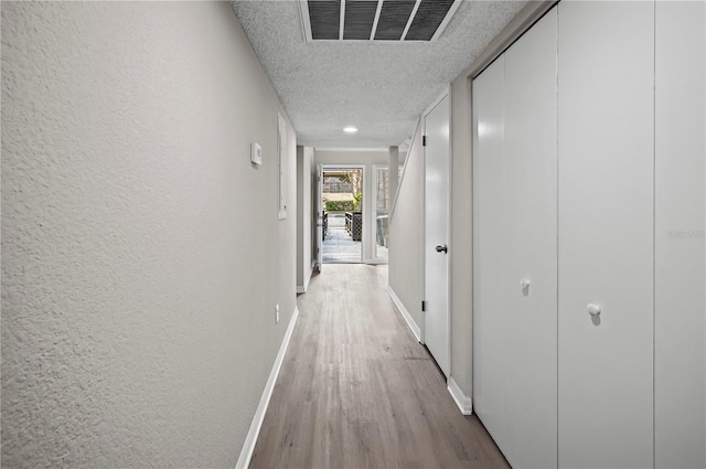 hallway with light wood-type flooring and a textured ceiling