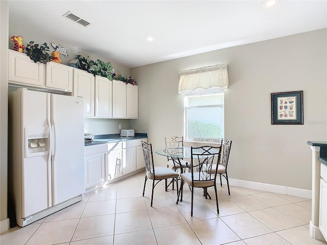 kitchen with white refrigerator with ice dispenser, white cabinetry, and light tile patterned flooring