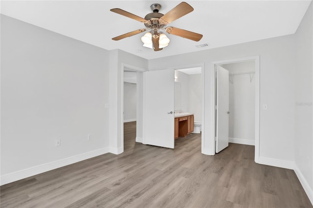 unfurnished bedroom featuring ensuite bath, ceiling fan, a spacious closet, light hardwood / wood-style floors, and a closet