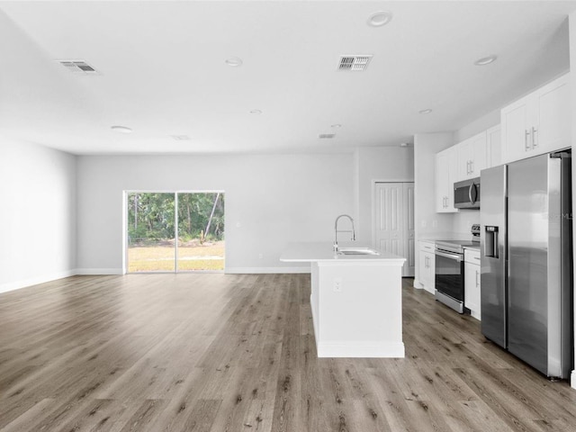 kitchen featuring appliances with stainless steel finishes, light wood-type flooring, sink, white cabinets, and an island with sink