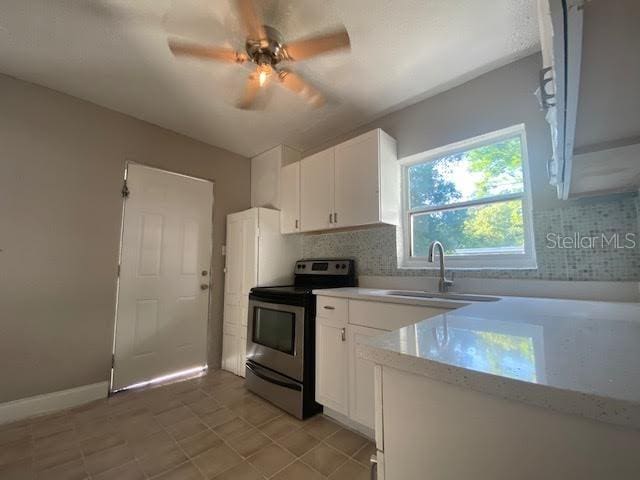 kitchen featuring tasteful backsplash, light countertops, white cabinets, a sink, and stainless steel electric range