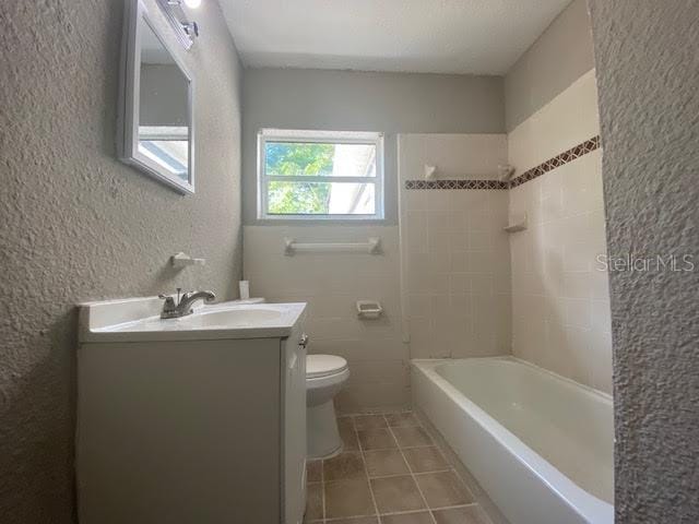 bathroom with shower / bathtub combination, a textured wall, toilet, vanity, and tile patterned floors