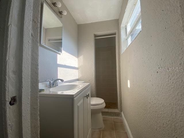 bathroom with toilet, a textured wall, tile patterned floors, and vanity