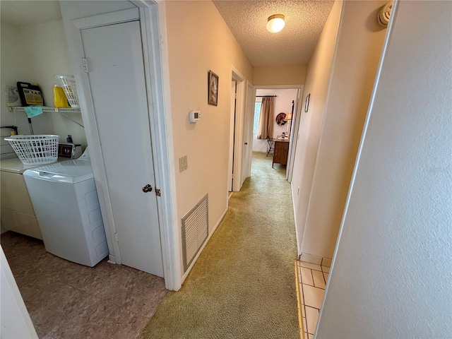 hallway featuring separate washer and dryer, light colored carpet, and a textured ceiling