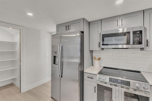 kitchen with gray cabinetry, light hardwood / wood-style flooring, stainless steel appliances, and tasteful backsplash