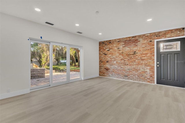 spare room with light hardwood / wood-style floors and brick wall