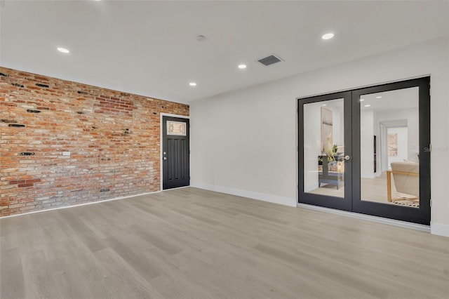 spare room featuring french doors, brick wall, and light wood-type flooring