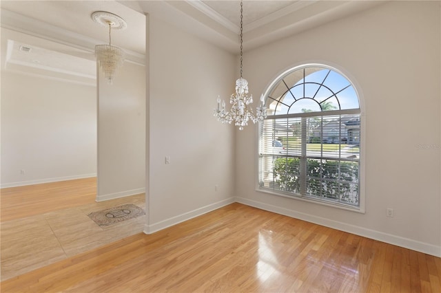 unfurnished room featuring hardwood / wood-style flooring, a raised ceiling, ornamental molding, and an inviting chandelier