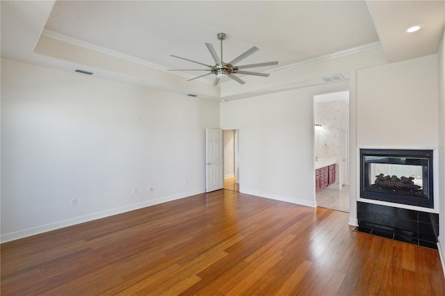 unfurnished living room featuring a tray ceiling, ceiling fan, crown molding, a multi sided fireplace, and hardwood / wood-style floors