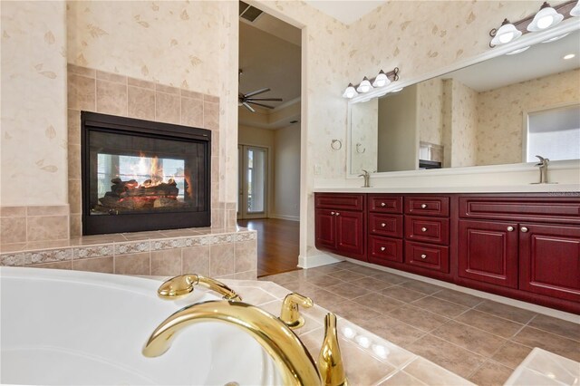 bathroom with vanity, ceiling fan, a multi sided fireplace, tile patterned flooring, and a tub