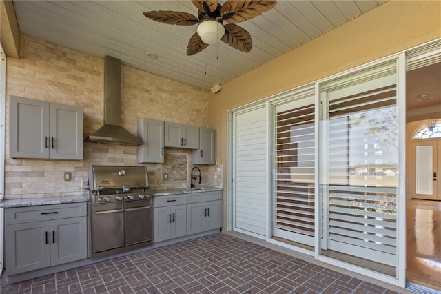 kitchen with ceiling fan, wall chimney exhaust hood, light stone counters, gray cabinets, and decorative backsplash