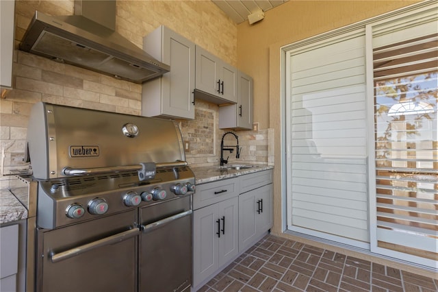 kitchen with gray cabinetry, backsplash, sink, wall chimney exhaust hood, and light stone countertops