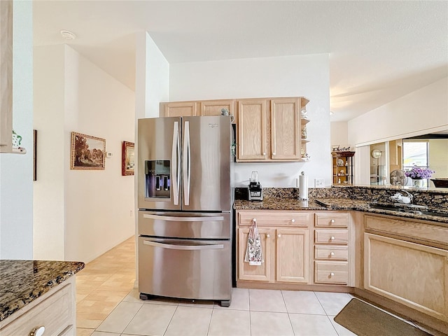 kitchen featuring dark stone counters, sink, light tile patterned floors, light brown cabinetry, and stainless steel fridge with ice dispenser