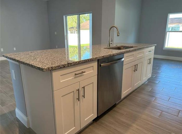 kitchen featuring a center island with sink, sink, stainless steel dishwasher, light stone counters, and white cabinetry