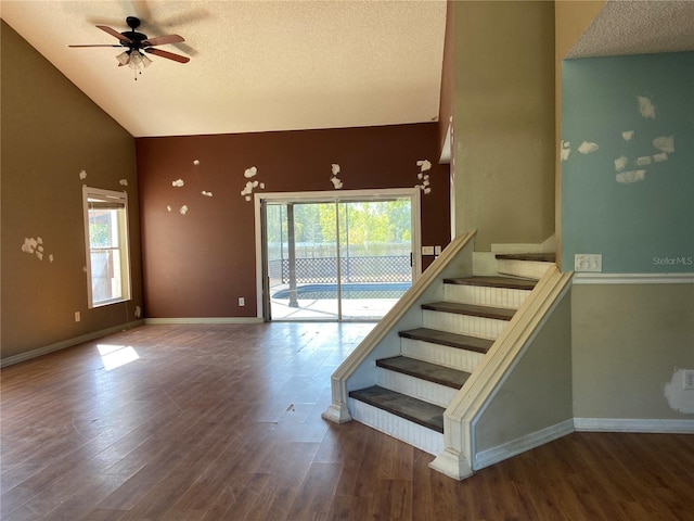 stairs with ceiling fan, high vaulted ceiling, a textured ceiling, and hardwood / wood-style flooring