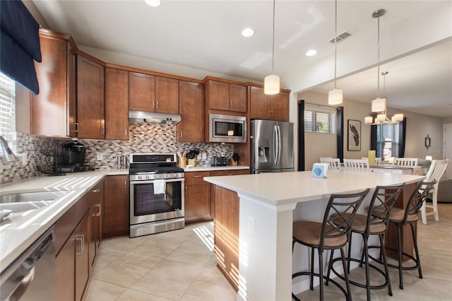 kitchen with a breakfast bar, stainless steel appliances, pendant lighting, a chandelier, and a kitchen island