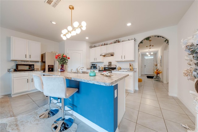 kitchen featuring appliances with stainless steel finishes, a kitchen island with sink, decorative light fixtures, a notable chandelier, and white cabinets