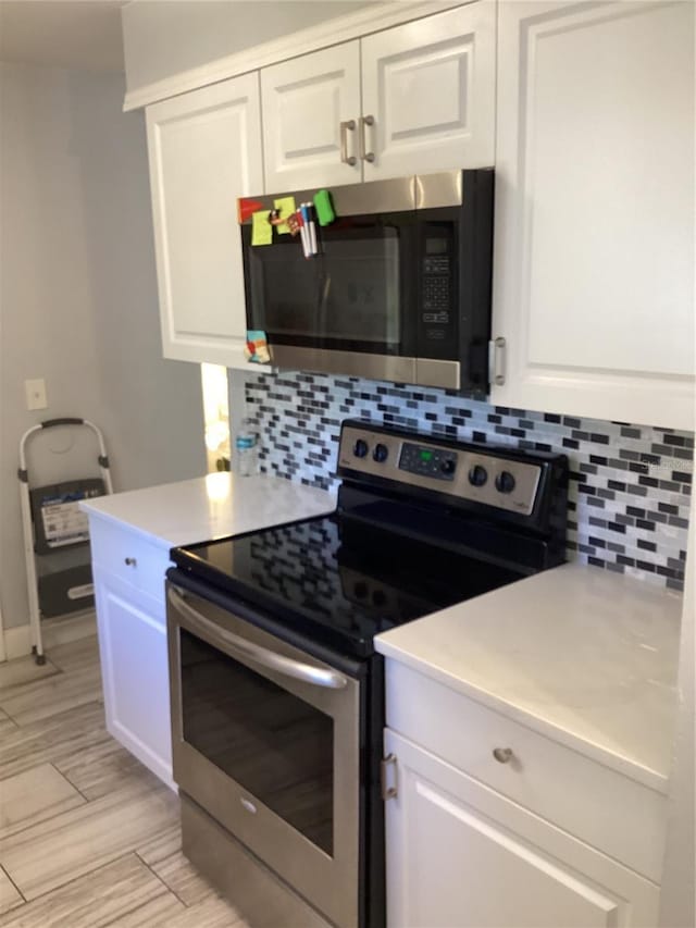 kitchen with stainless steel appliances, wood finish floors, white cabinetry, light countertops, and tasteful backsplash