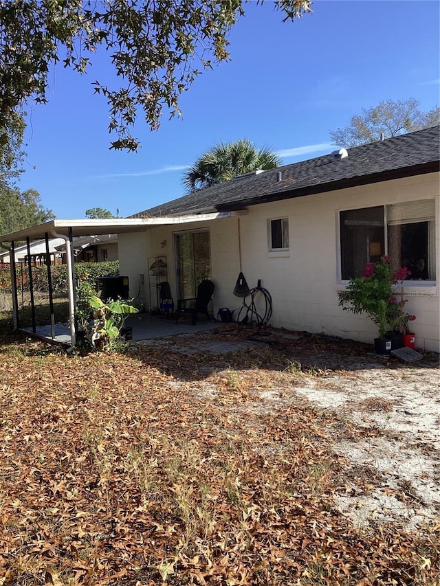 view of side of property with a shingled roof, a patio area, and concrete block siding