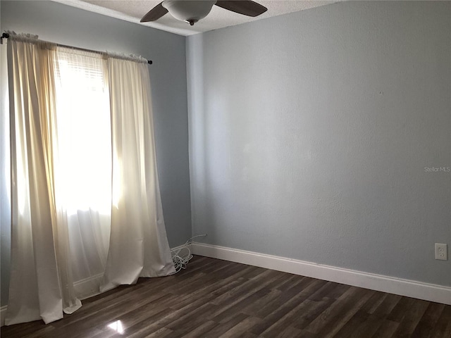 spare room featuring dark wood finished floors, a ceiling fan, and baseboards