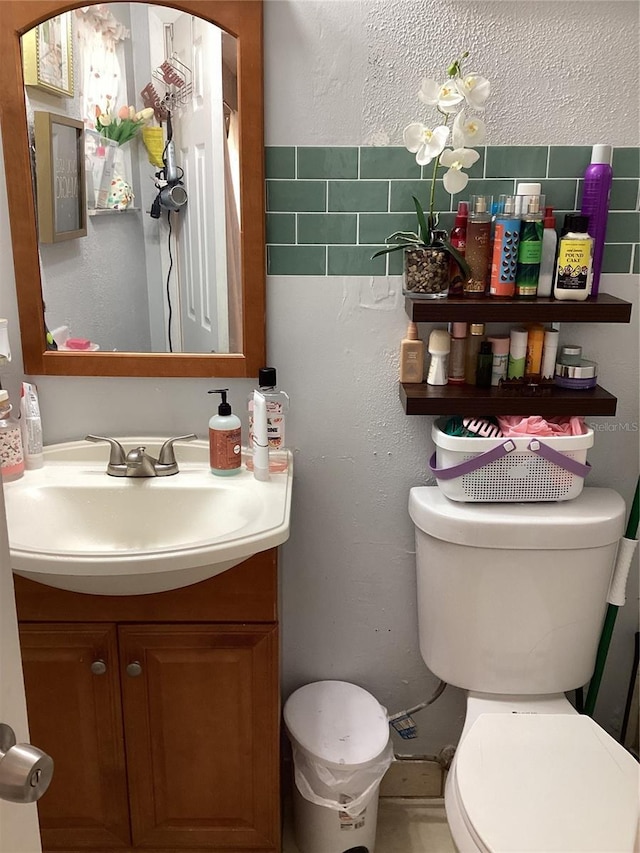 half bathroom featuring toilet, vanity, and a textured wall