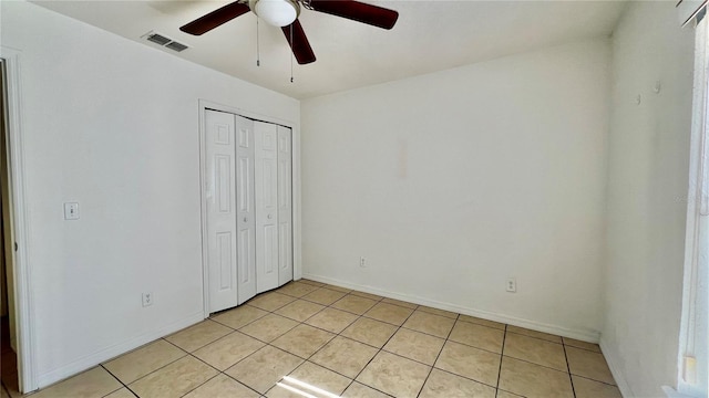 unfurnished bedroom featuring light tile patterned floors, visible vents, baseboards, a ceiling fan, and a closet