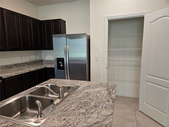 kitchen featuring stainless steel fridge with ice dispenser, sink, light tile patterned floors, and light stone countertops