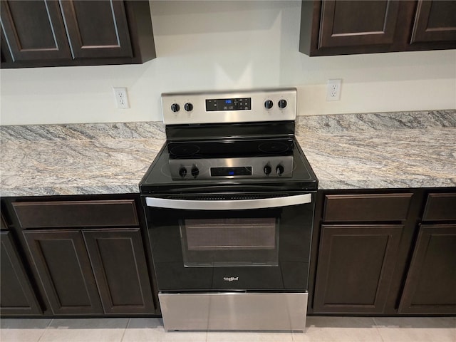 kitchen with dark brown cabinetry, light stone countertops, light tile patterned flooring, and stainless steel electric range