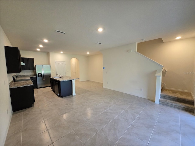 kitchen featuring stainless steel refrigerator with ice dispenser, light stone counters, sink, light tile patterned floors, and an island with sink