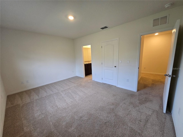 unfurnished bedroom featuring light carpet, ensuite bathroom, and a closet