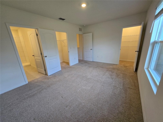 unfurnished bedroom featuring light colored carpet, a spacious closet, connected bathroom, and a closet