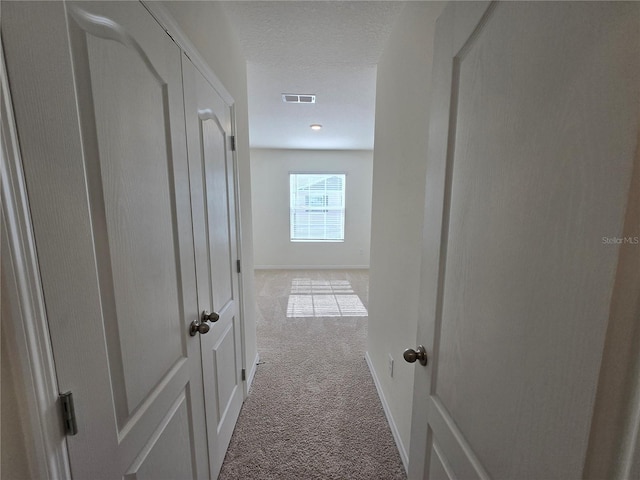 corridor featuring light colored carpet and a textured ceiling