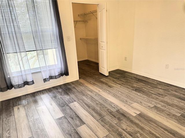 unfurnished bedroom with a walk in closet, dark wood-type flooring, and a closet