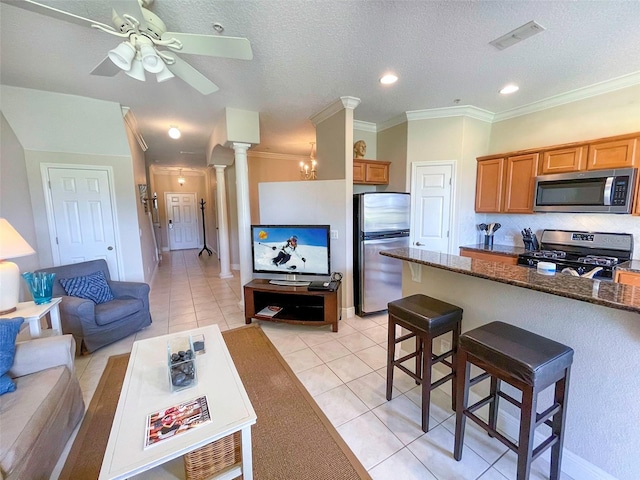 kitchen with appliances with stainless steel finishes, ornate columns, a textured ceiling, light tile patterned floors, and a breakfast bar area