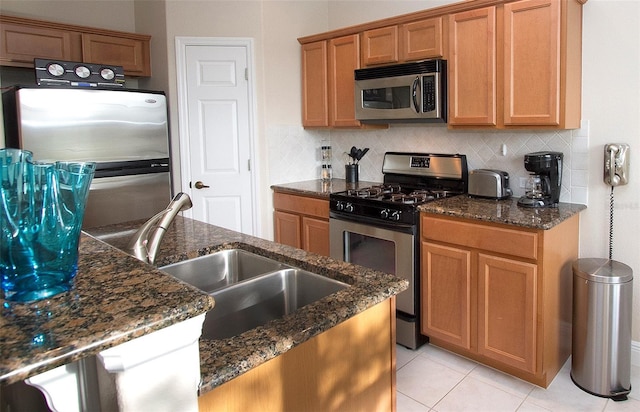 kitchen with sink, decorative backsplash, dark stone countertops, light tile patterned floors, and stainless steel appliances