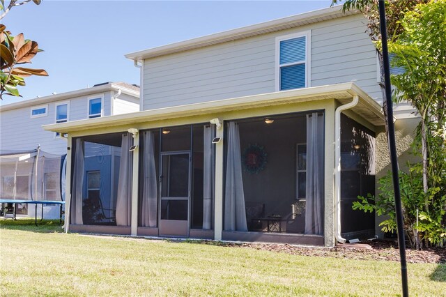 back of house featuring a sunroom, a trampoline, and a yard