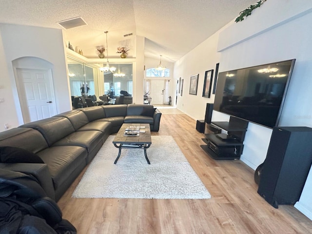 living room with a textured ceiling, light hardwood / wood-style floors, an inviting chandelier, and vaulted ceiling