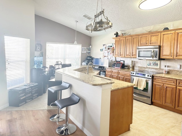 kitchen featuring lofted ceiling, a kitchen island with sink, decorative light fixtures, a kitchen bar, and stainless steel appliances