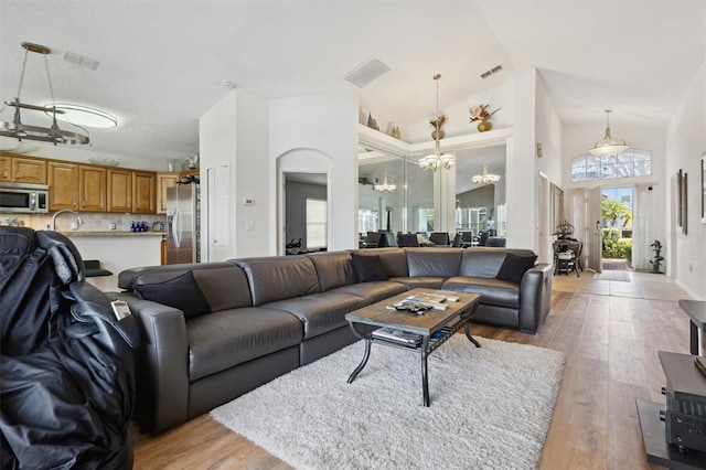 living room with high vaulted ceiling, sink, an inviting chandelier, and light hardwood / wood-style floors