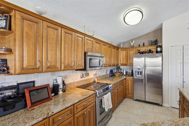 kitchen featuring decorative backsplash, vaulted ceiling, light stone countertops, and appliances with stainless steel finishes